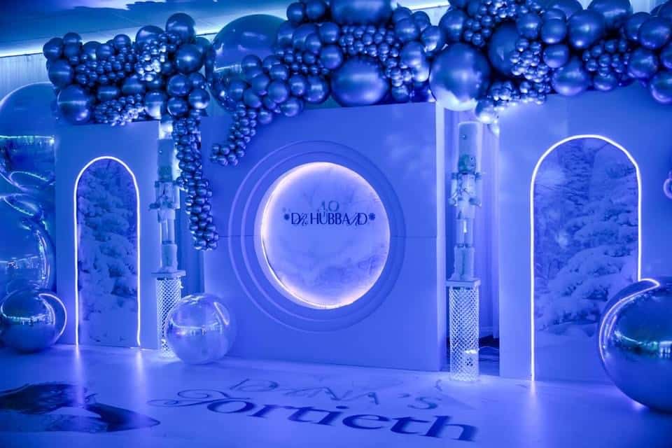 A themed event space decorated with silver and blue balloons, featuring round and arched doorways, along with wintery landscape images and decorative globes. the floor displays the text "dar's gortech.