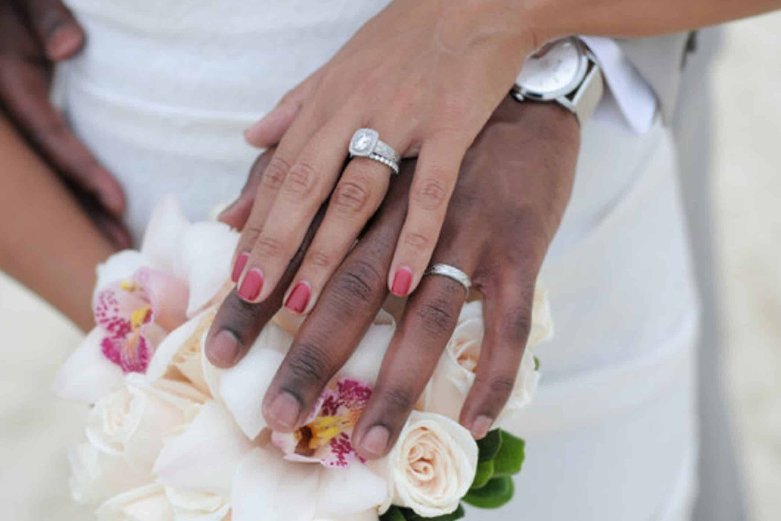 Close-up of a bride and groom's hands over a wedding bouquet, showcasing their wedding rings. the image focuses on their hands and the delicate decoration of the bouquet.