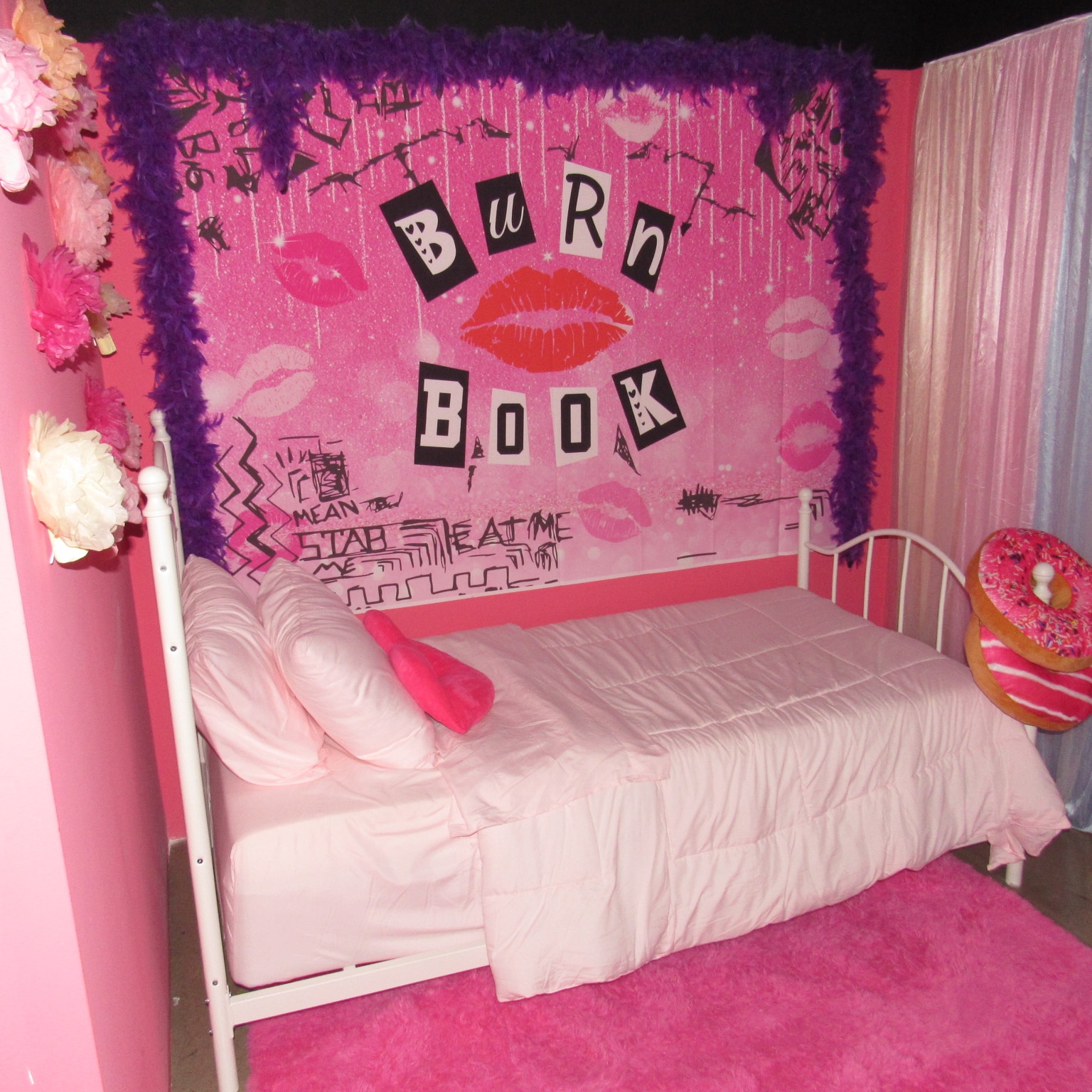A vibrant pink-themed bedroom with a single bed, pink bedding, and a "burn book" themed headboard. the room features pink curtains, a fluffy rug, and decorative flowers.