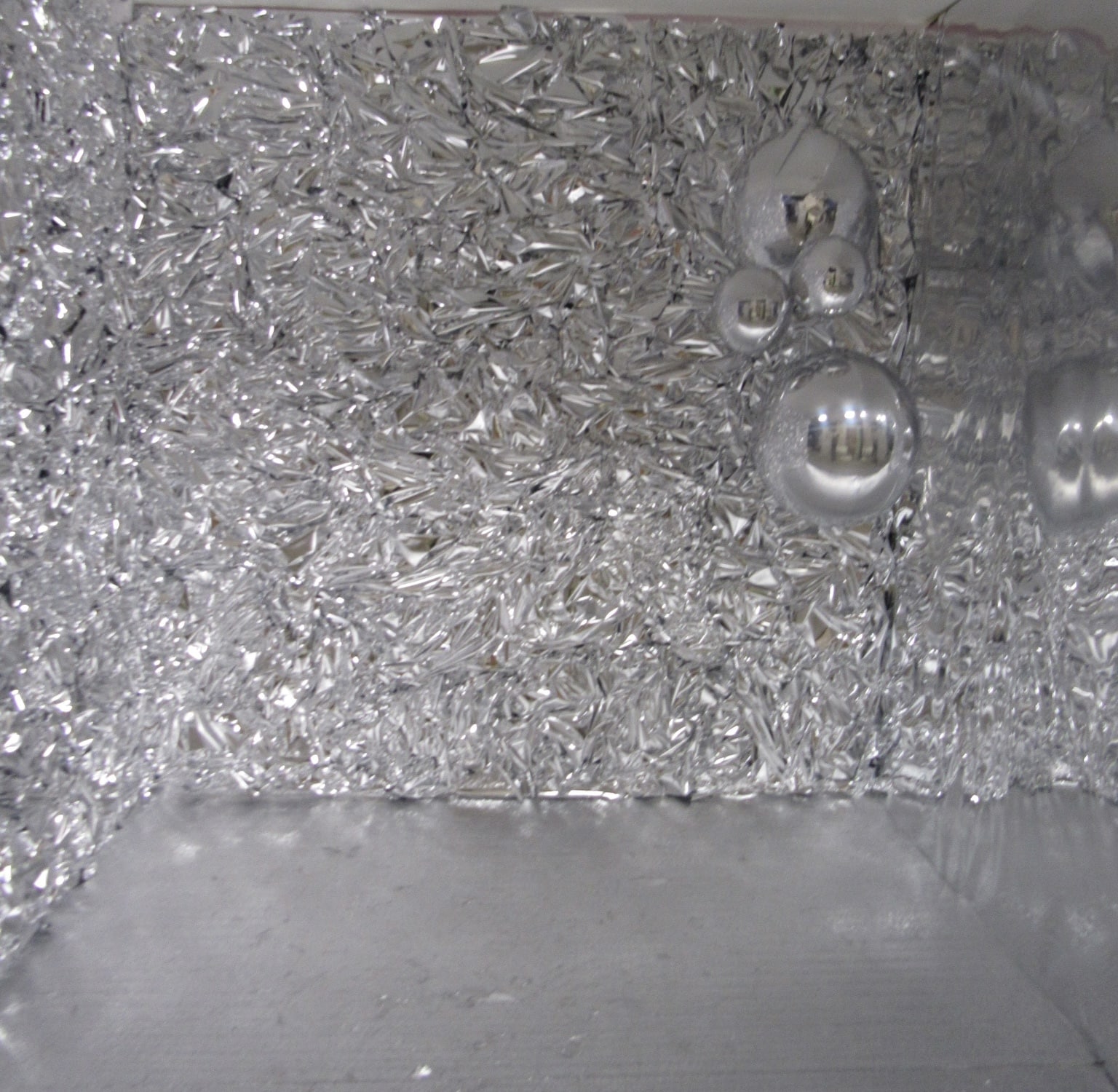 A close-up view of a reflective surface strewn with tiny metallic confetti pieces, and interspersed with a few larger, round, shiny silver ornaments.