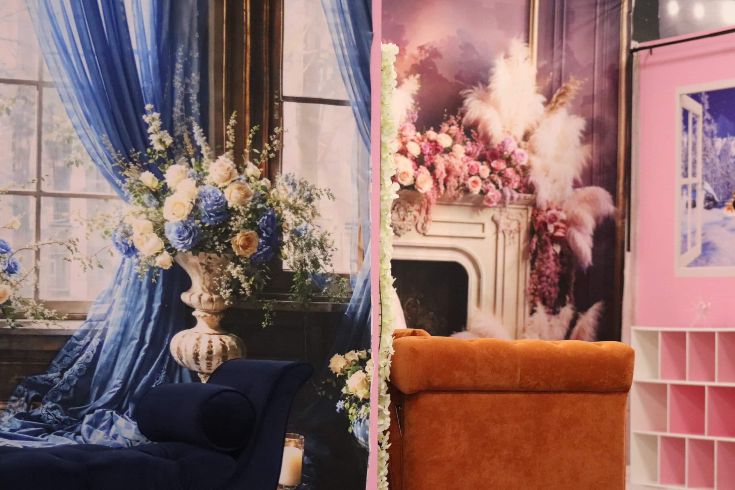 Elegant interior design display featuring a bedroom with a plush blue bed and draped blue curtains, accented by floral arrangements, next to a pink-themed room with a floral fireplace.