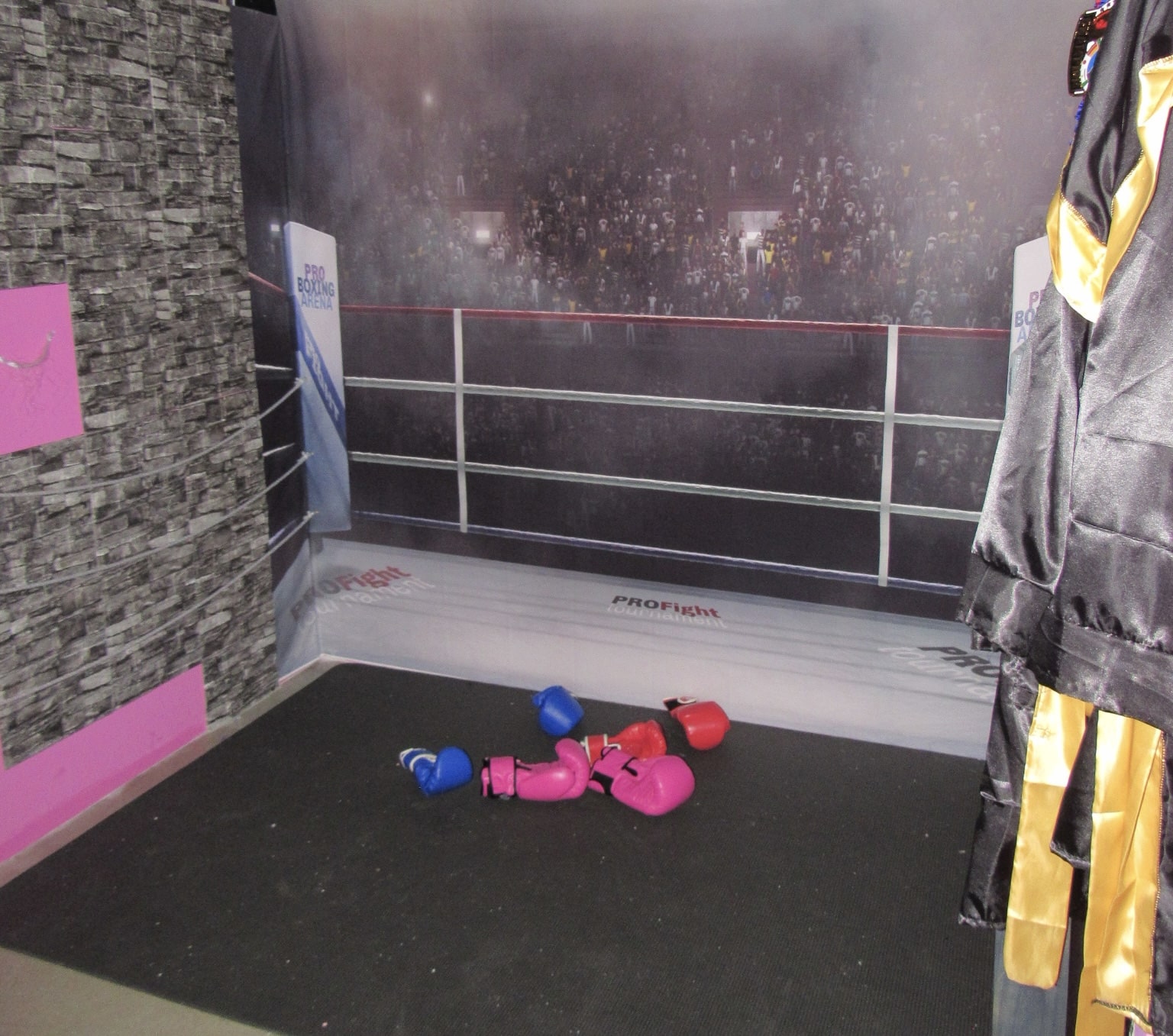 An exhibition display featuring boxing gloves and a robe, with a sports arena crowd in the background depicted on a large photo. the setting includes gray walls and a carpeted floor.